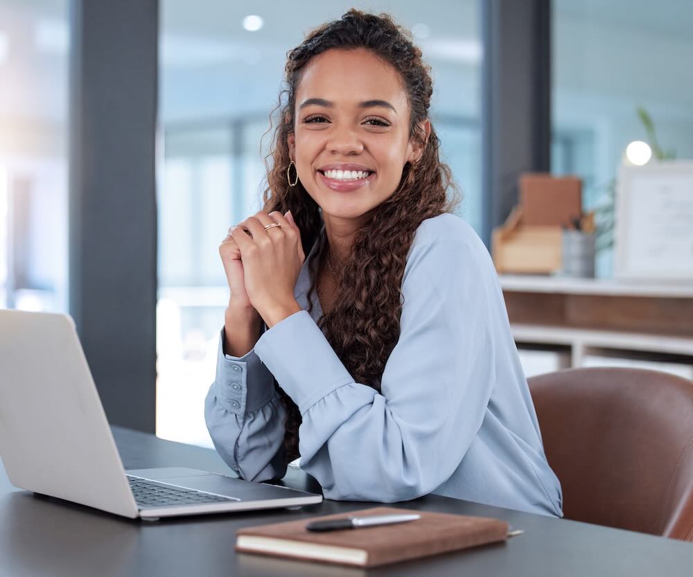 Young woman sitting at her desk smiling looking at a camera